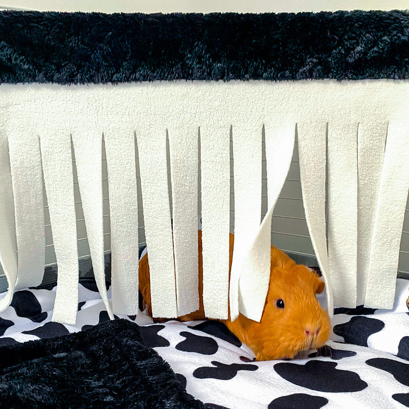 a ginger guinea pig hiding behind a kavee black corner hide on top of cow print fleece