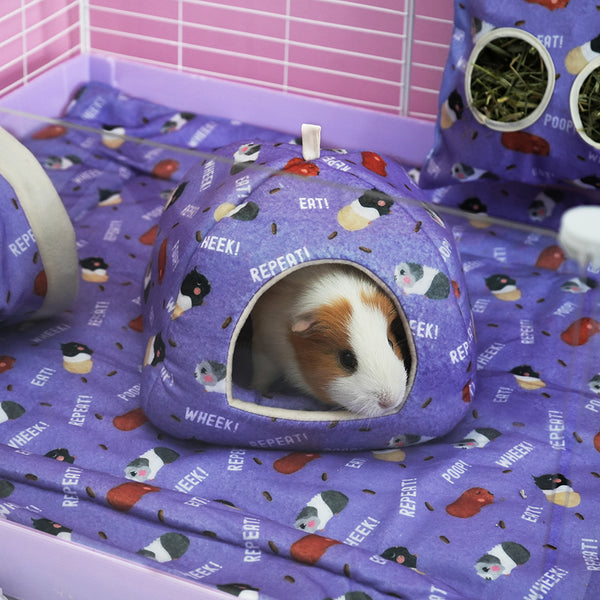 Purple fleece poop design hidey house with a white and brown guinea pig inside placed on a purple fleece liner pig inside white cage with liner, tunnel haybag and grids in background by brand Kavee