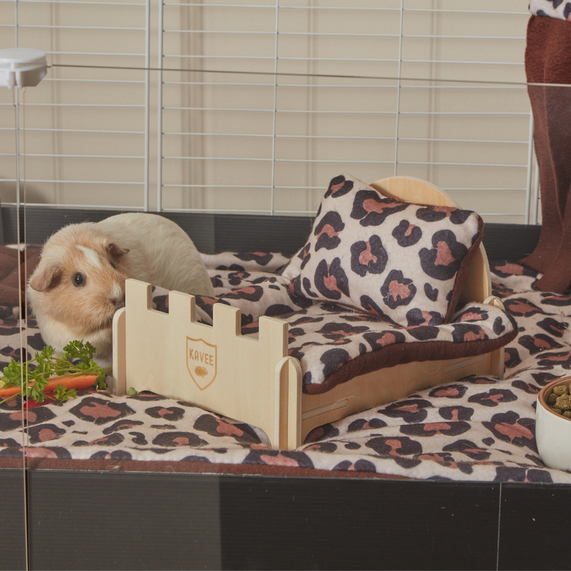 a ginger and white guinea pig next to a kavee wooden bed with leopard print pillow and pee pad on top